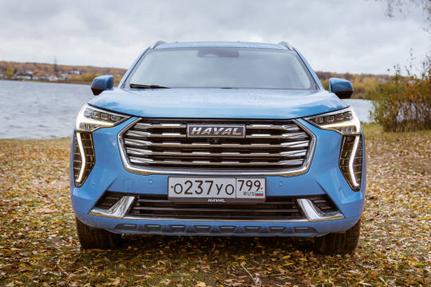 Вид спереди синего кроссовера Haval Dargo, припаркованного на травяной площадке рядом с водоемом.